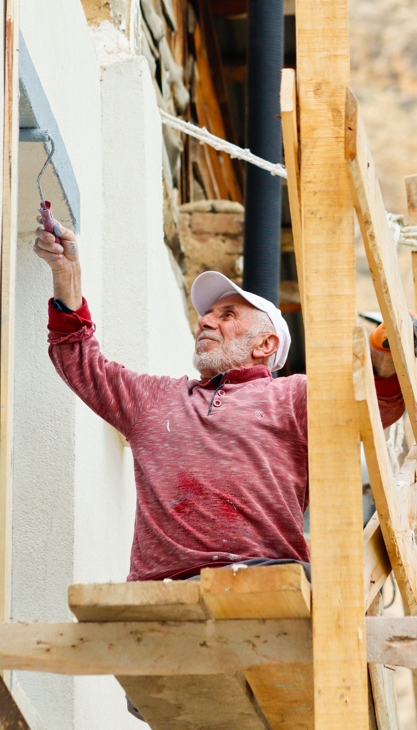 A painter on scaffolding rolling paint onto an exterior stucco wall