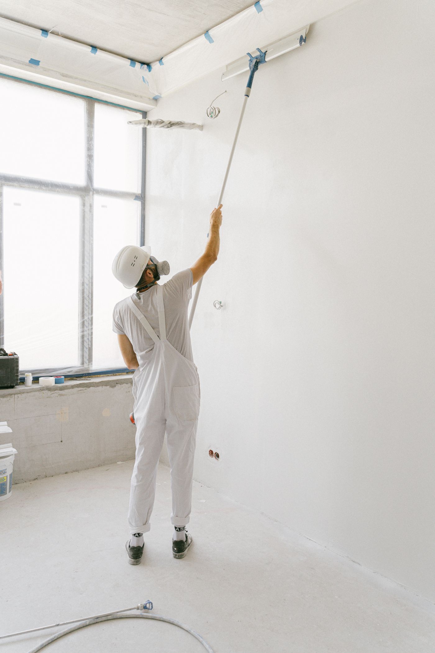 A painter in white overalls rolling paint on an interior wall