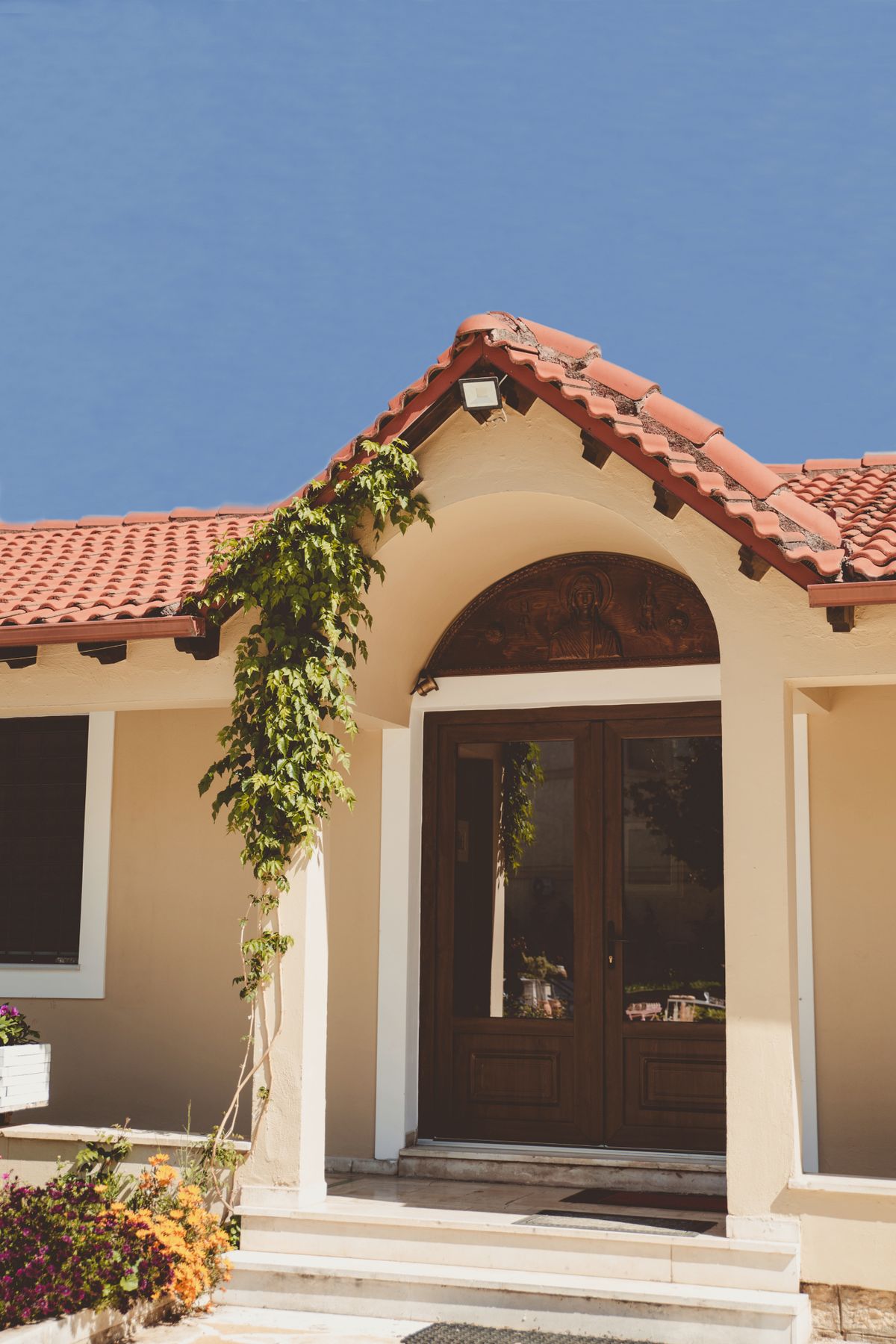 Cream stucco entry with a clay tile roof under a blue sky