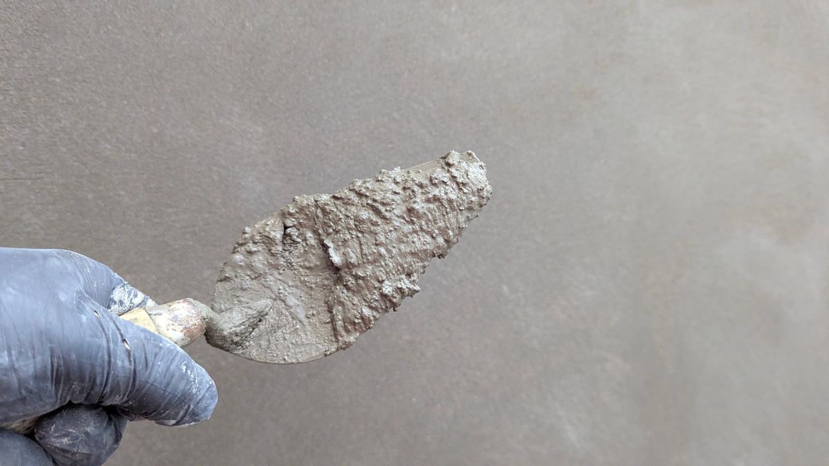 Gloved hand holding a trowel of fresh stucco against a wall